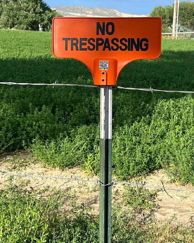 Safety-orange Whack-A-Sign No Trespassing sign posted on a T-post along a farm fence line